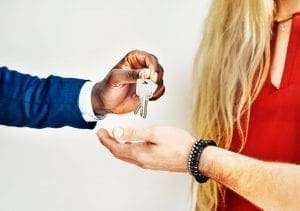 a black estate agent handing over keys to a young blonde woman and her partner