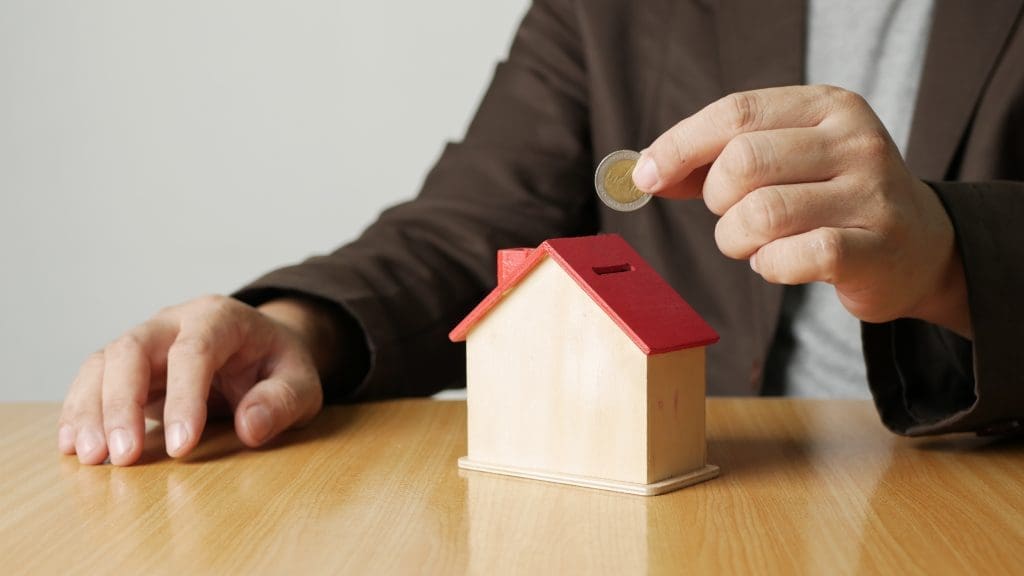 Close-up shot of a person placing a coin into a wooden model of a house