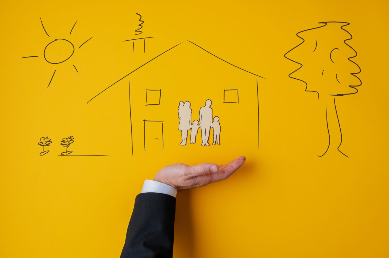 Male hand in a suit in supportive gesture under a hand drawn house with a paper cut silhouette of a family inside in conceptual image. Over yellow background.