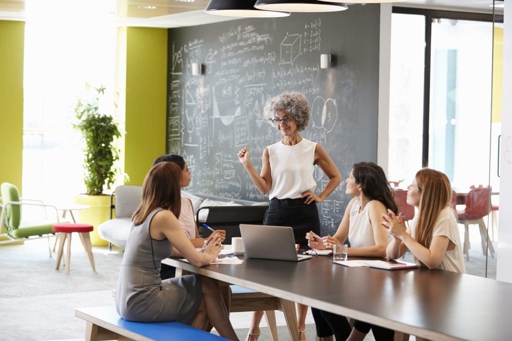 Female boss standing at an informal team meeting with four other women. 