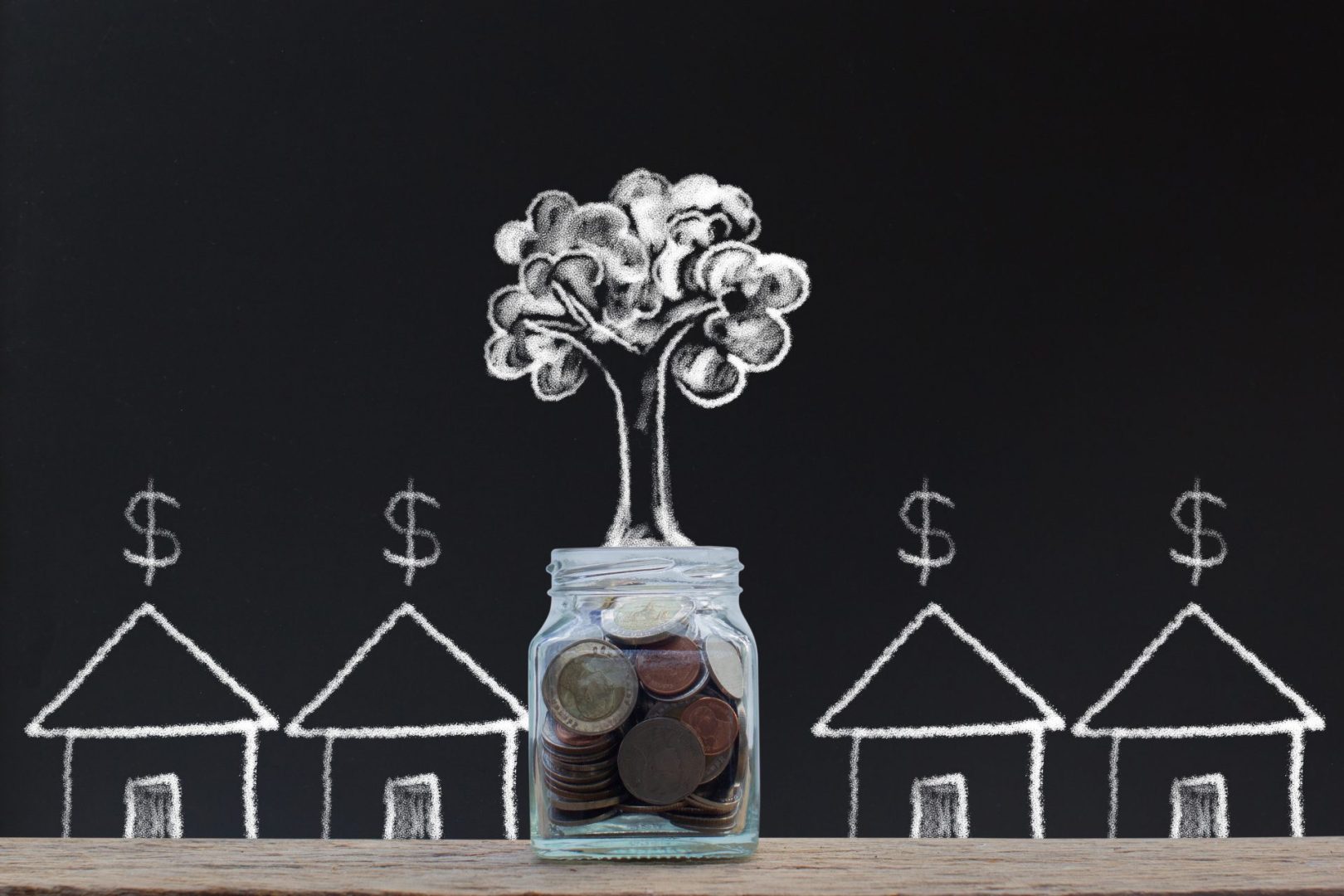 Savings money. Money investment concepts. Home loan. hand drawing stacking coins in glass jar and growing tree with small residents on chalkboard.