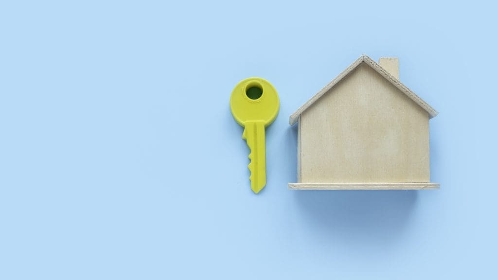 Key beside a house model. Blue background with copy space.