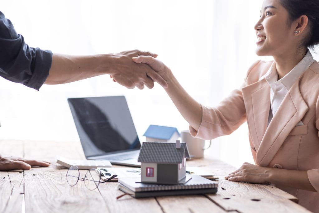Mortgage broker shakes hand with a customer, sample home model is placed on the desk between them