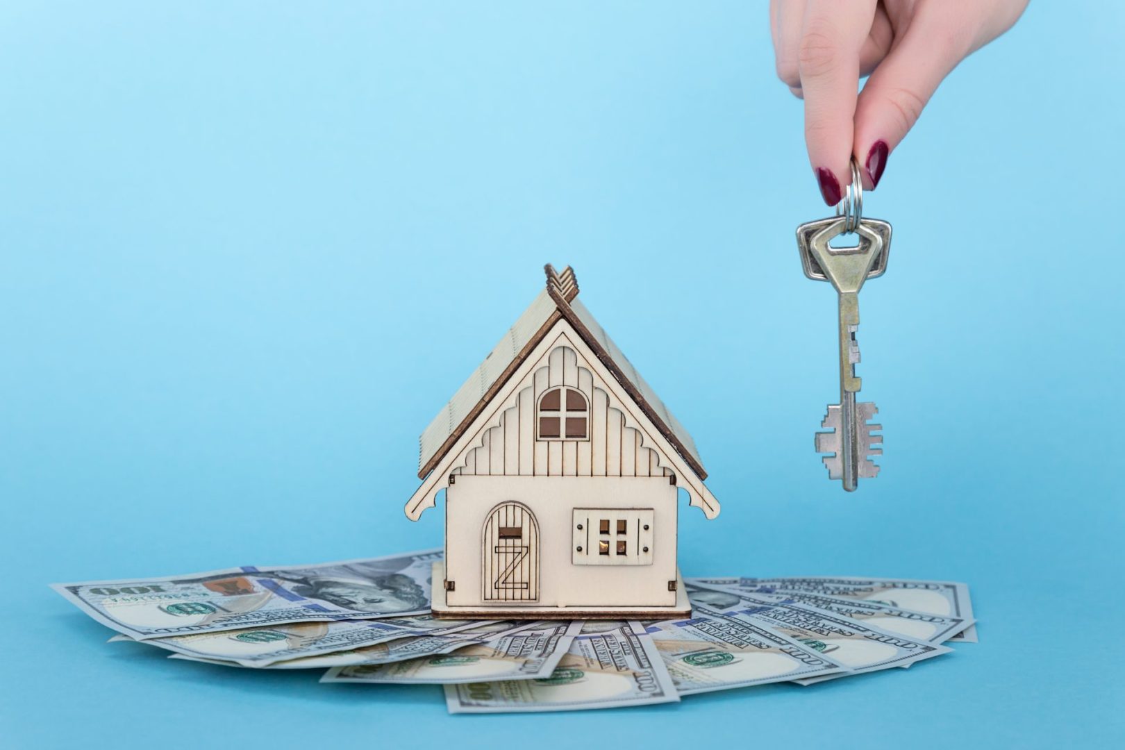 a bunch of keys and a toy house standing on a pile of money on a blue background