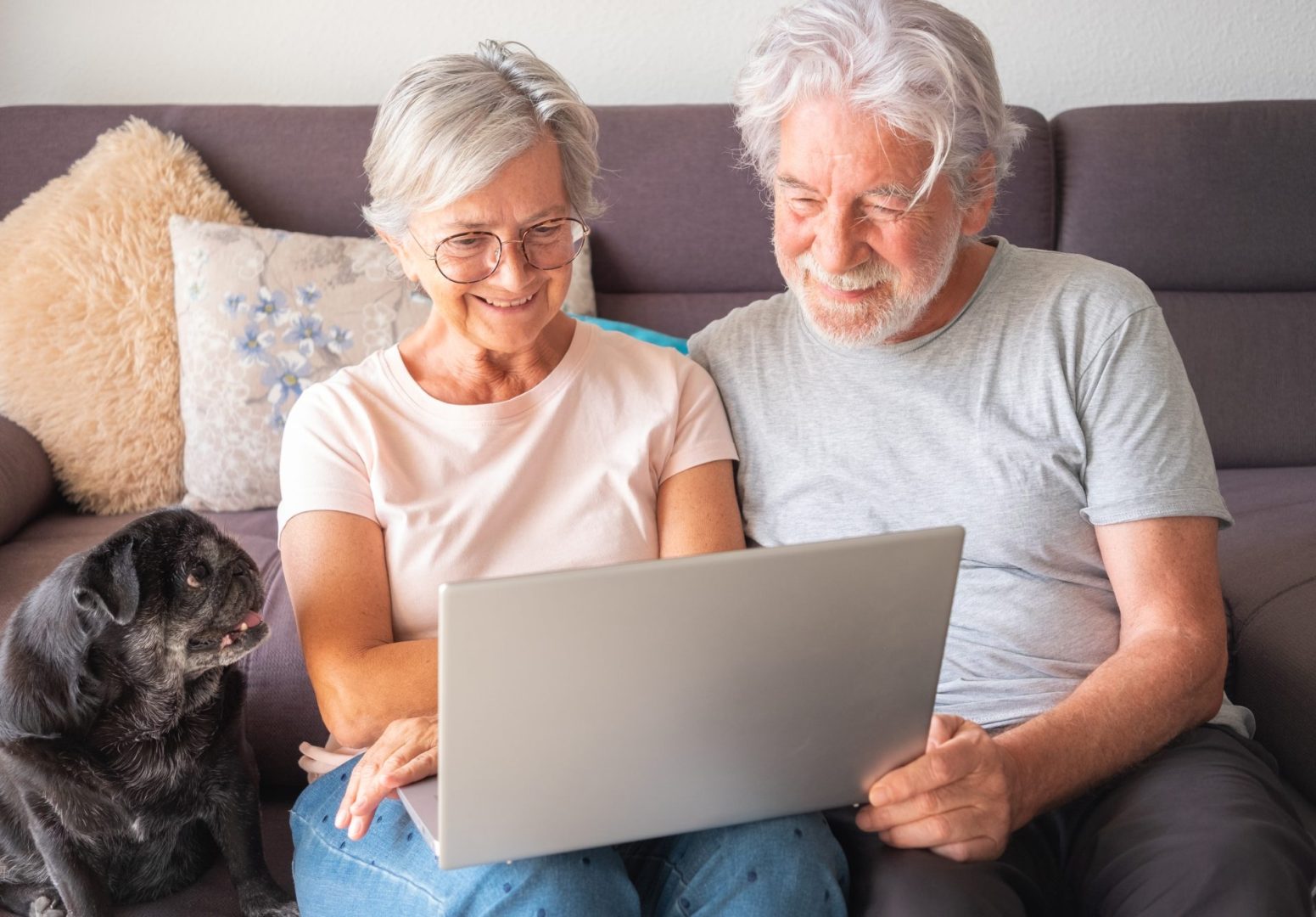 Portrait of senior Caucasian couple with old pet pug dog having good time together at home on a laptop