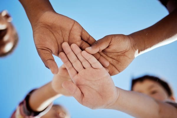 stack of hands and children in unity, support or solidarity with a blue sky background.
