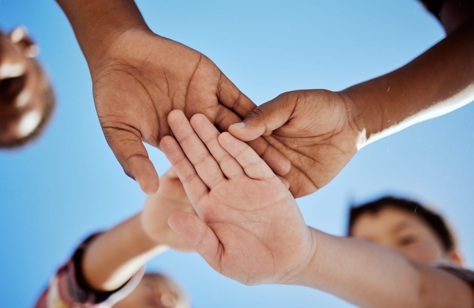 stack of hands and children in unity, support or solidarity with a blue sky background.