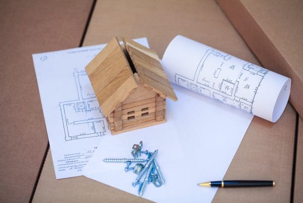 Wooden house model resting on papers with building instructions for new homes