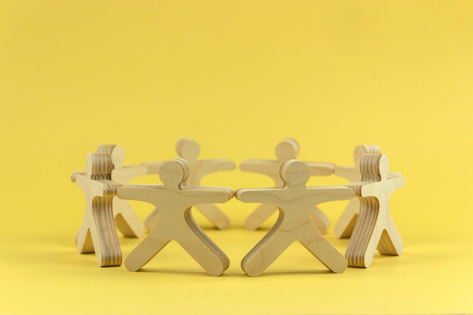 wooden figures stood holding hands in a circle. Yellow background